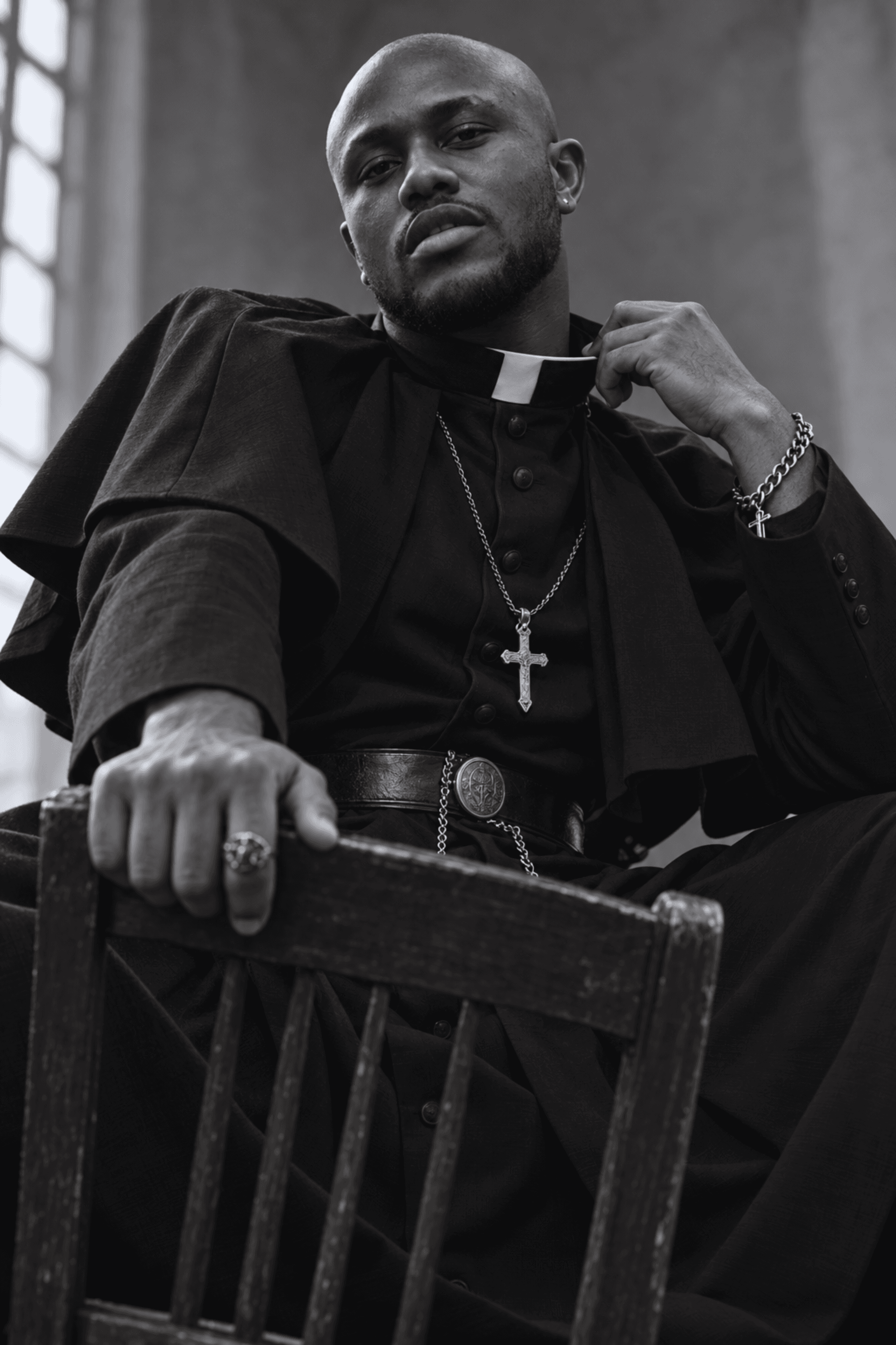 Muiz as a priest in black robes, seated on a chair
